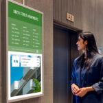 Woman looking at digital signs next to an elevator.