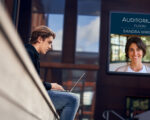 Boy sitting in public sector area with computer and a digital sign.